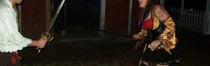 Man woman in pirate costumes sword fighting